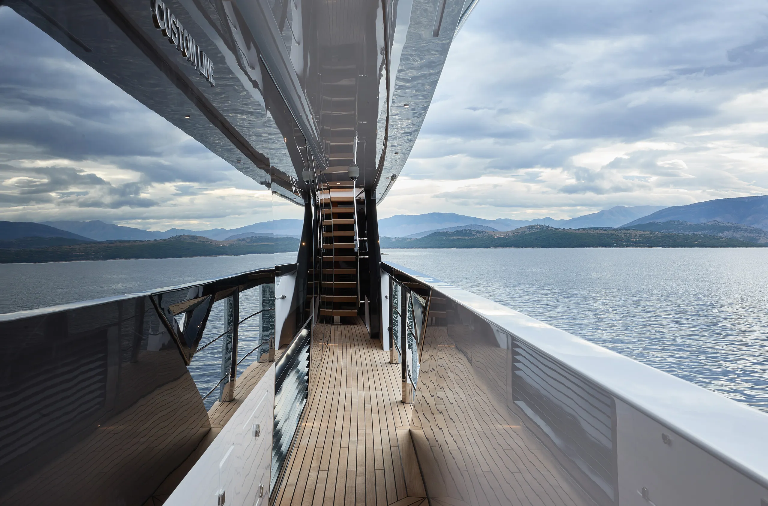 A side deck onboard the Custom Line 106 superyacht, there is a moody sky reflected in the side details of the boat
