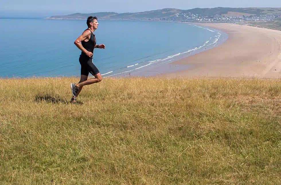 A man running along the Devon coast as part of the Devon Triathlon series, Croyde Beach is in the background
