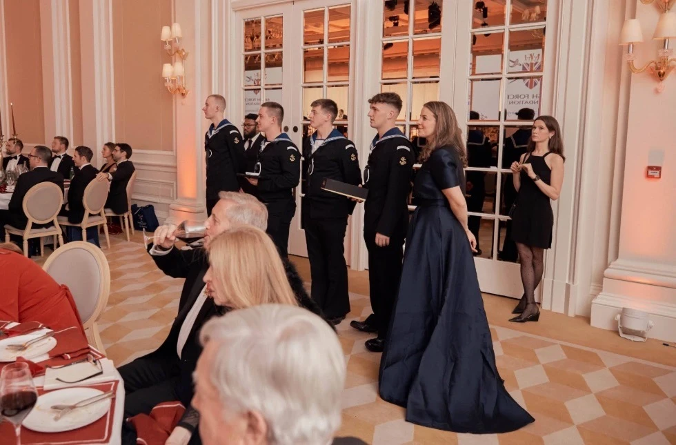 A lady in a navy evening gown standing with a group of naval cadets