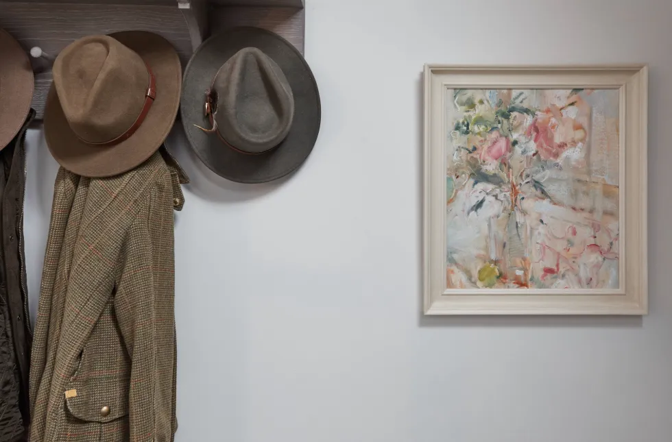 A picture of some hats and coat hanging next to a piece of art from Wychwood Art